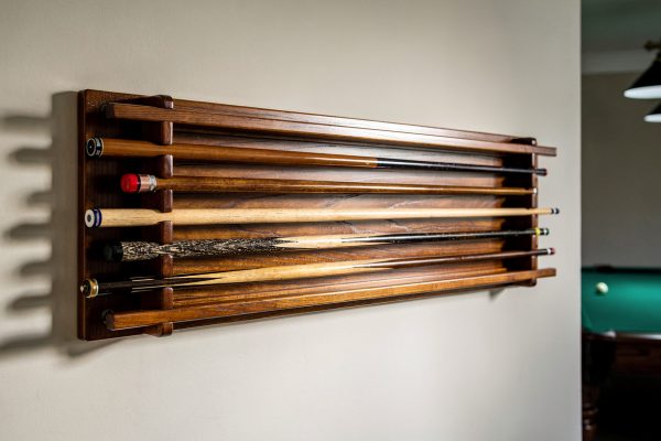 Wall-mounted wooden pool cue holder rack with multiple cues stored horizontally in game room