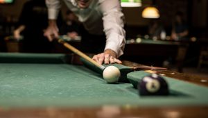 Pool player executing a kick shot to escape trouble with cue ball rebounding off the rail